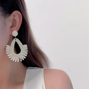 Detail of handmade cream woven raffia drop earrings with fringe on a model for beach style