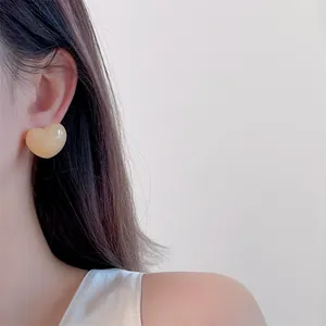 Close-up of a model wearing cream yellow heart-shaped stud earrings in a minimalist style