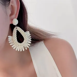 Detailed close-up of woven raffia teardrop earrings on a model for beach vacation style
