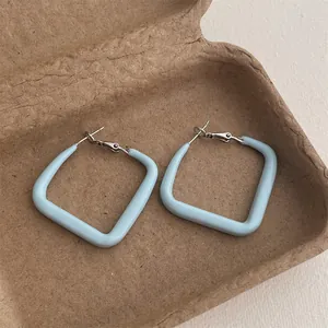Detail view of light blue square lacquer earrings on a textured brown eco-friendly tray