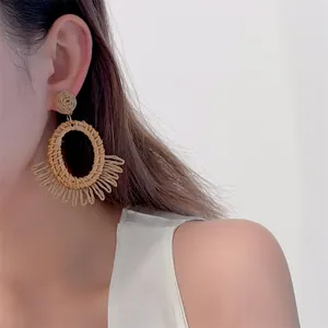 Detailed view of handmade raffia earrings with natural woven circles and fringe on model