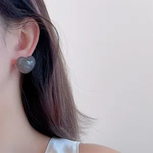 Close-up of a glossy dark grey heart-shaped resin earring shown on a model's ear