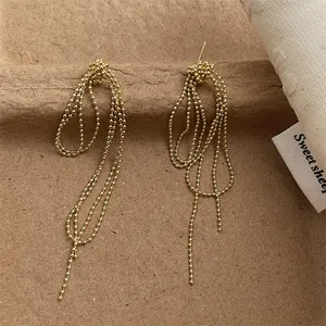 Detail of gold beaded tassel earrings with layered chain drop on vintage background
