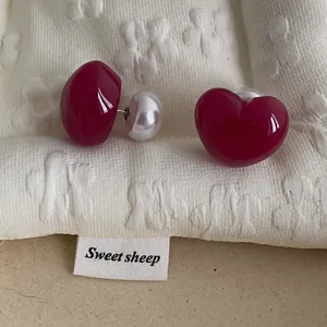 Macro shot of asymmetrical deep red glazed heart earrings with large white pearl backings