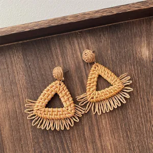 Detail of handmade raffia earrings with woven triangles and fringe on dark wood