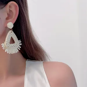 Close-up of handmade raffia earrings with triangular fringe and woven texture on model