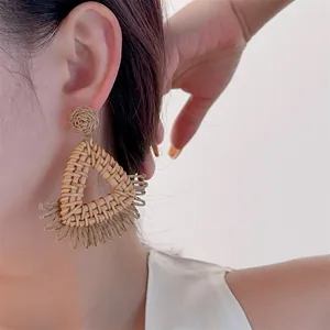 Close-up of bohemian hand-woven raffia earrings with triangle drop and straw tassels