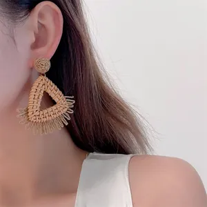 Macro detail of triangle straw woven earring with circular tassels for beach vacation style