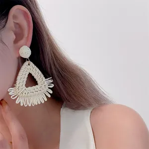 Detail of hand-woven straw tassel earrings in cream white for beach vacations