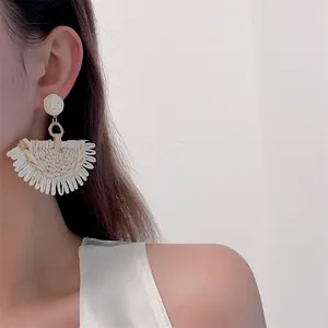 Detail of handmade raffia fan earrings in ivory, worn by a model in a bohemian style