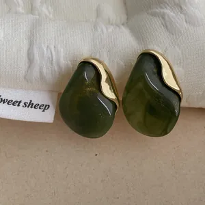 Macro view of dark green resin earrings with gold flecks and metallic border detail