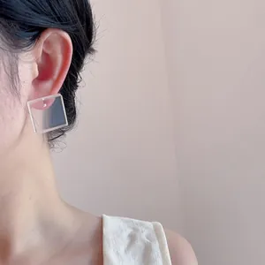 Close-up of a minimalist clear acrylic square stud earring worn by a model in profile view