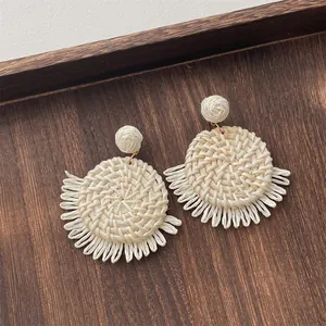 Detail of cream handmade raffia earrings with woven texture and fringe on wood