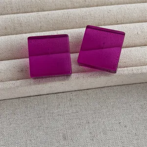 Detailed view of square magenta acrylic stud earrings on a textured display stand