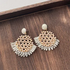 Close-up of handmade raffia earrings with peach beads and woven fringe details