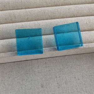 Detail of square blue acrylic stud earrings on a beige linen jewelry display tray