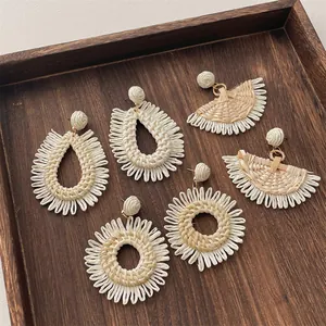 Close-up of handmade raffia earrings in drop, fan, and hoop shapes on a wooden tray