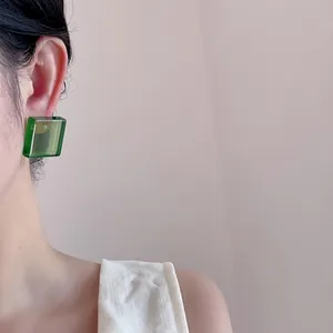 Detail shot of a transparent green acrylic cube earring worn by a model in soft light