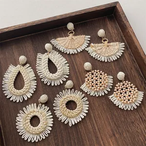 Detail view of woven raffia earrings in various bohemian styles on a dark wooden tray