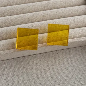 Detailed view of translucent yellow acrylic cube earrings on a linen texture display
