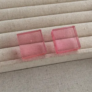 Detail shot of pink acrylic cube stud earrings on a beige linen jewelry display tray