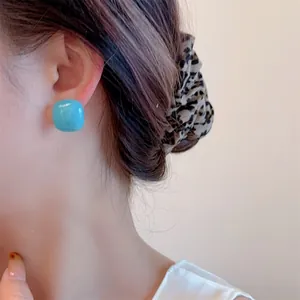 Close-up of a model wearing bright blue square resin studs with a glossy glazed finish