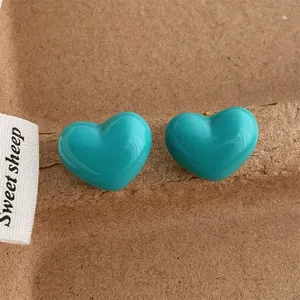 Close-up of bright turquoise heart-shaped stud earrings on a brown paper background