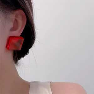 Detail of a bright red transparent acrylic cube stud earring worn on the ear model