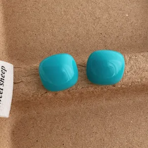 Detailed view of glossy cyan square heart stud earrings on a rustic brown paper background