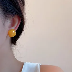 Detailed view of vibrant yellow candy-colored square resin stud earrings on earlobe