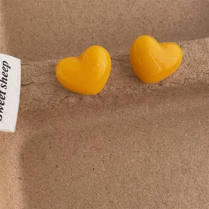 Close-up of bright yellow 3D heart stud earrings on a textured brown fiber tray