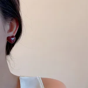 Close-up of a model wearing a glossy deep red heart stud earring with a minimalist style