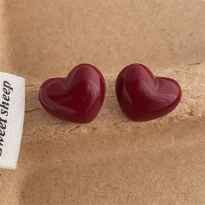 Macro shot of glossy burgundy heart-shaped stud earrings on a textured paper background