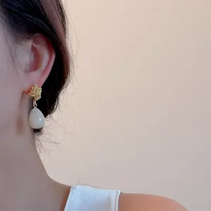 Detail of vintage gold textured stud and teardrop pearl earring on a female model