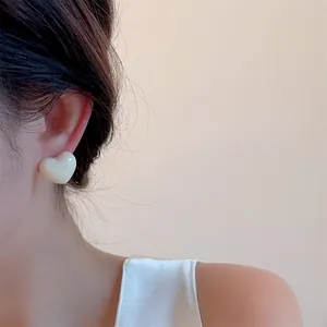 Close-up of a model wearing cream-colored heart-shaped earrings with a ceramic-like finish