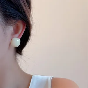 Close-up of cream square stud earrings with a glossy finish on a model's ear