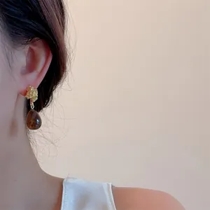 Close-up of olive water drop earrings with irregular gold studs and amber resin charms