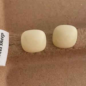 Close-up of cream-colored square resin stud earrings on textured brown paper