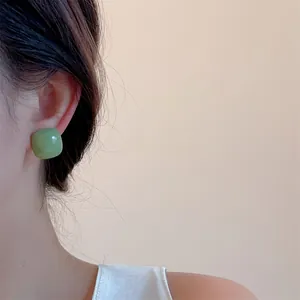 Close-up of a model wearing square candy-colored green heart stud earrings in resin