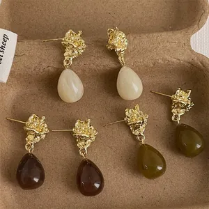 Close-up of vintage metal and acrylic teardrop earrings in olive, cream, and brown