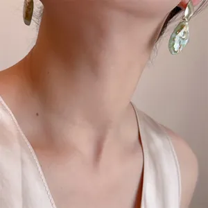 Eleganti orecchini dorati con pendente a goccia verde menta indossati da una modella