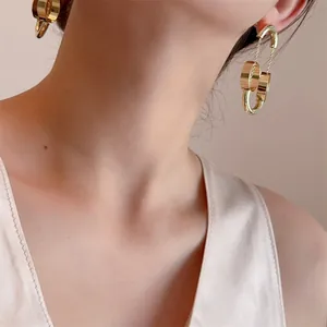 Dettaglio di lunghi orecchini geometrici dorati con ganci a U indossati da una modella