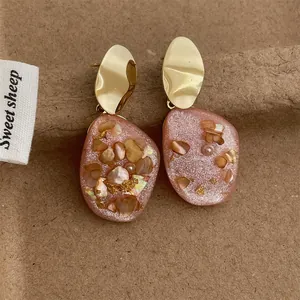 Dettaglio di orecchini in resina rosa con frammenti di conchiglia e foglia d'oro