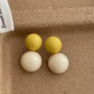 Vista macro di orecchini a bottone sferici minimalisti giallo senape e bianco crema