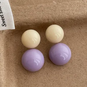 Dettaglio di orecchini retrò in resina a contrasto con doppie sfere crema e lavanda