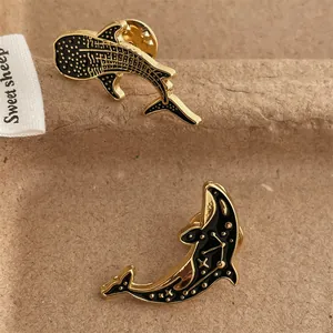 Detailed close-up of whale and dolphin enamel pins with gold plated edges on a brown card