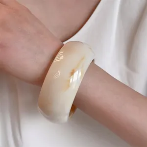 Detail of wide resin bangle with amber marble patterns on smooth cream surface