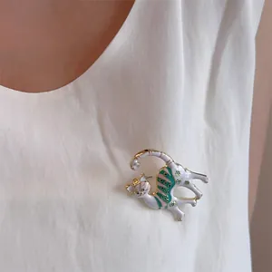 Detail einer süßen weißen Emaille-Katzenbrosche mit Goldrand auf weißer Kleidung