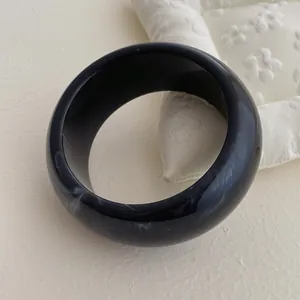 Macro shot of wide resin bangle with black and white marble texture on a soft surface