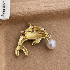 Back view of gold dolphin brooch with safety pin and hanging pearl detail